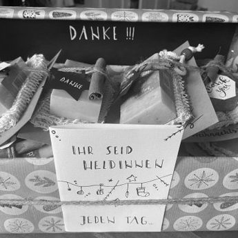 Bild von Frauenhausaktion Mitarbeiterinnengeschenk: Geschenkbox mit bunten Paketen und der Aufschrift „Danke!“ in Schwarz-Weiß.