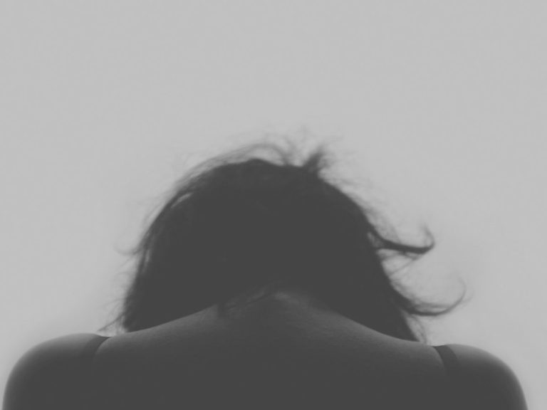 Eine silhouettierte Person mit gesenktem Kopf und fransigem Haar, in nachdenklicher Haltung.