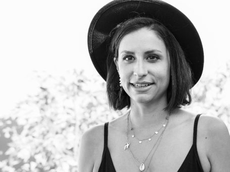 Alina Jessl mit kurzer brauner Haarfrisur, schwarzem Hut und mehrschichtigen Halsketten.