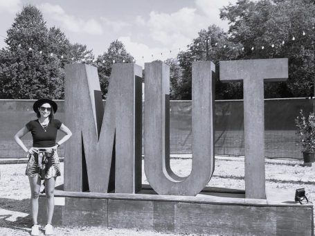 Alina Jessl steht neben großen, stilisierten Buchstaben „MUT“ im Freien.