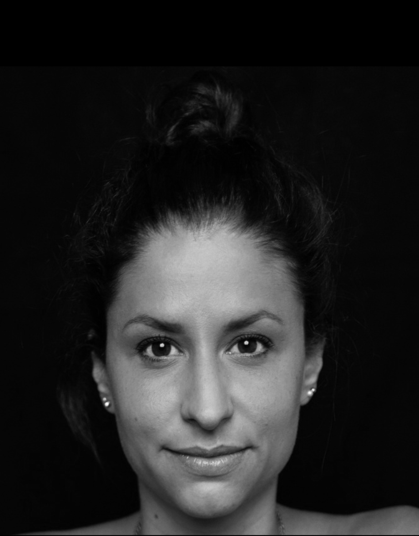 Porträt einer Frau mit dunklem Haar als Dutt, lächelnd und  vor schwarzem Hintergrund. Die Abbildung zeigt nur den Kopf, ist schwarz weiß